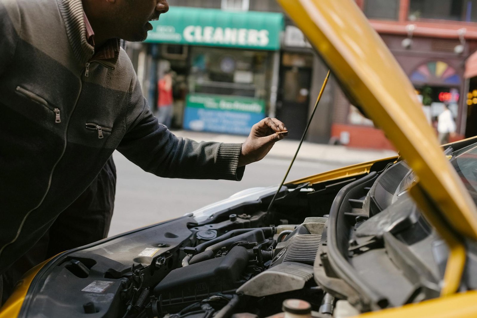 Mechanic examining car engine on a city street, highlighting vehicle maintenance.