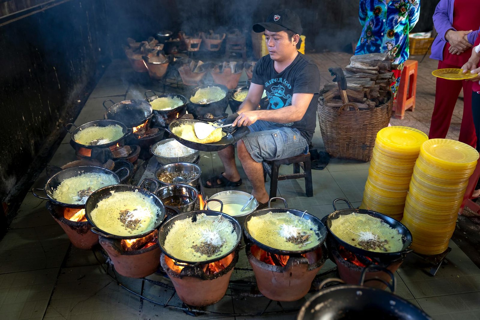 Street food vendor prepares traditional dishes using multiple cooking pots over open flames.
