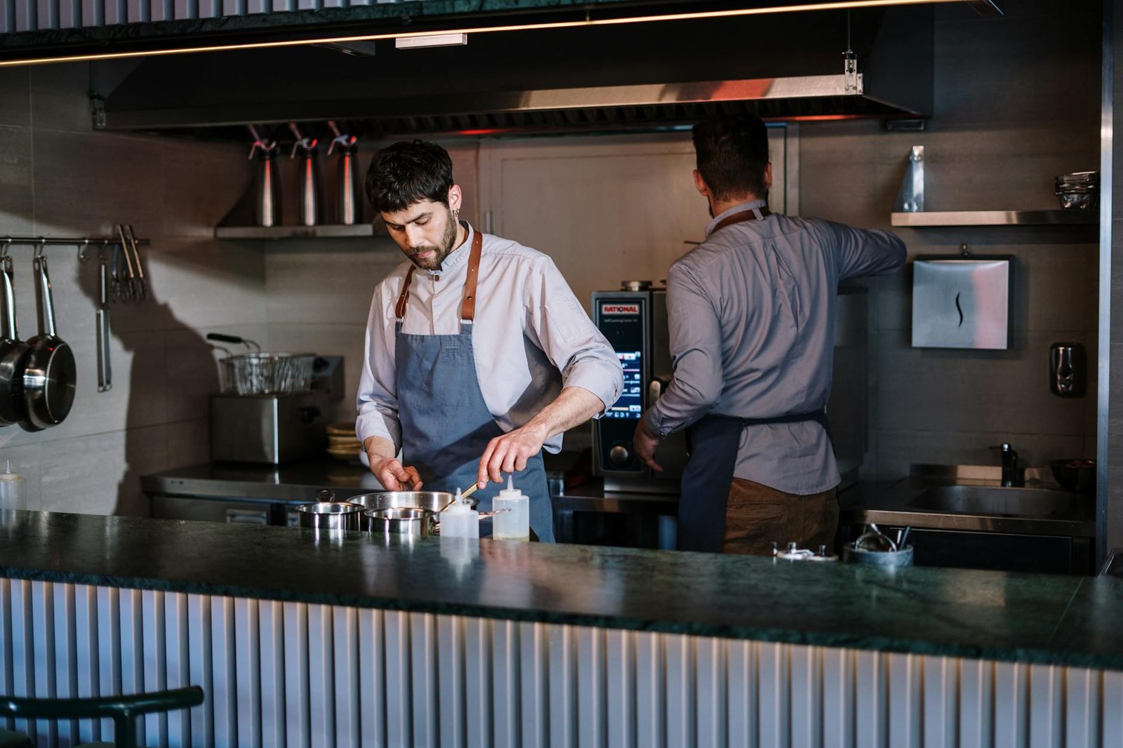 Two chefs working in an open kitchen, preparing dishes in a modern restaurant.