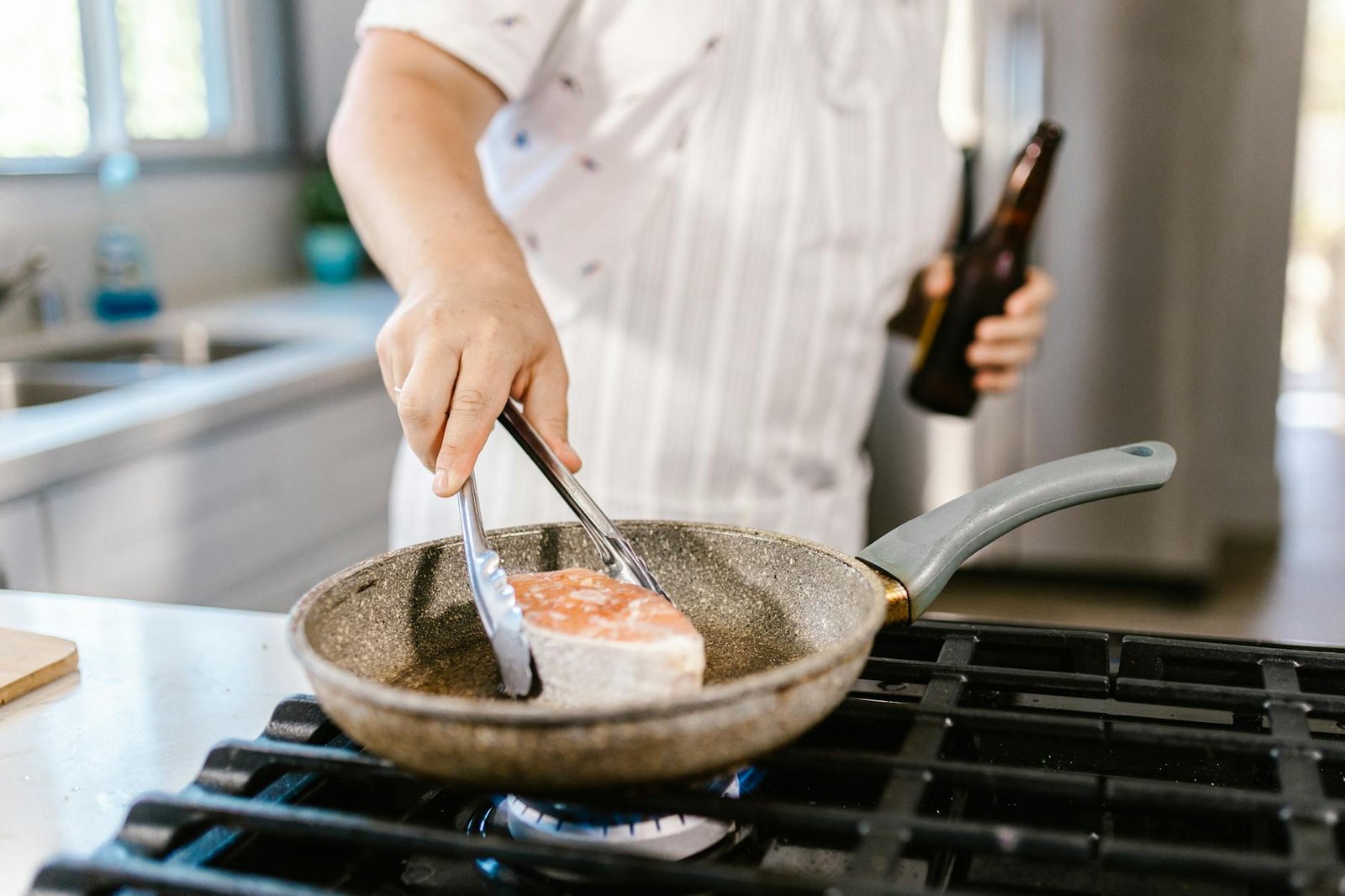 A person cooking salmon fillet in a frying pan on a kitchen stove.