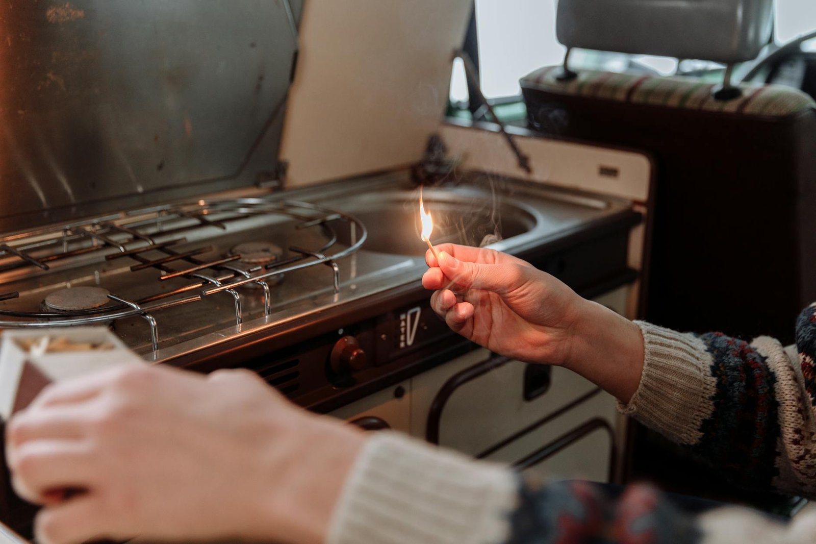 Close-up of hands lighting a matchstick near a stovetop in a cozy kitchen environment.