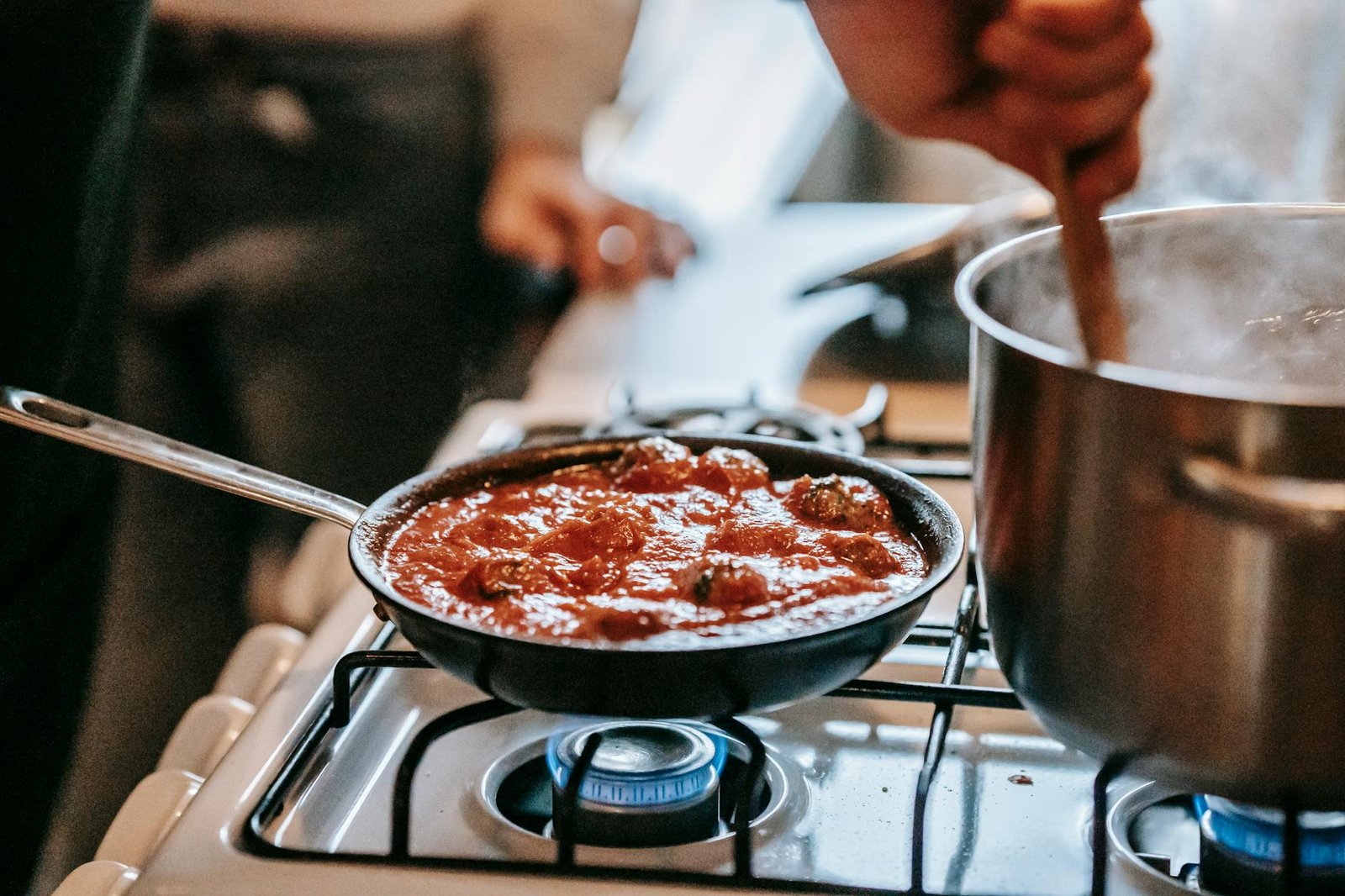 Debunking the High Heat Myth for Perfect Sear on Gas Stoves 5 Crop unrecognizable person stirring boiling water in saucepan placed on gas stove near frying pan with appetizing meatballs in tomato sauce