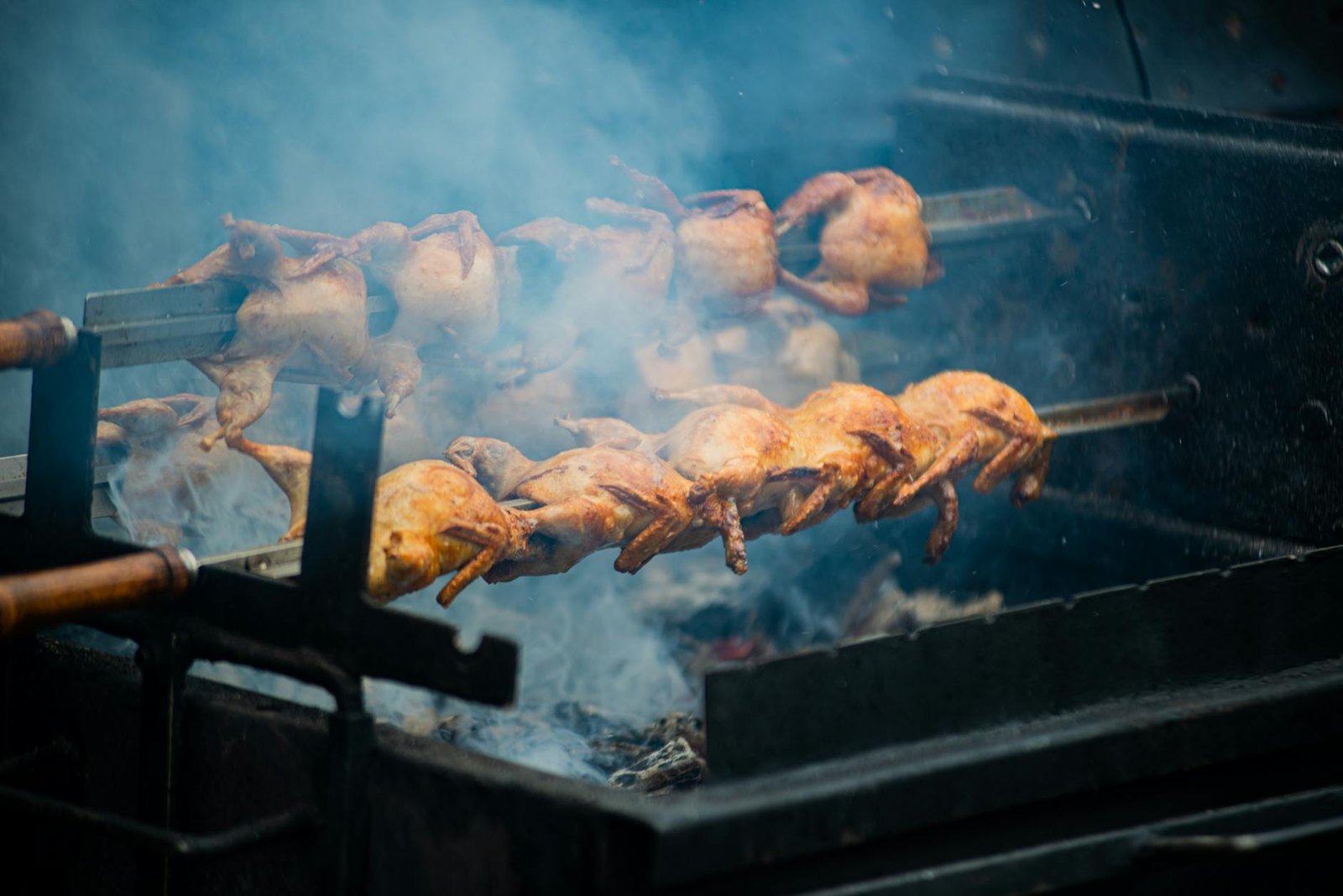Juicy whole chickens roasting on a spit over open flames outdoors, creating smoky flavors.