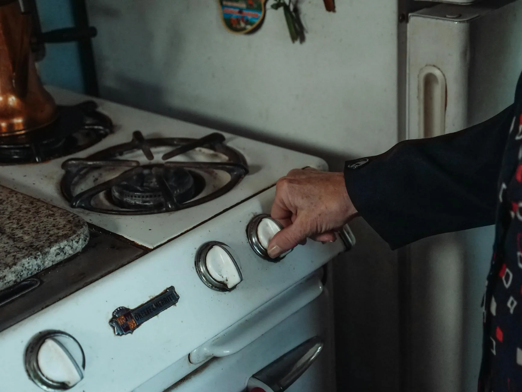 Hand adjusting an electric stove dial knob — the infinite switch behind every dial cycles power on and off, producing the faint click most owners hear