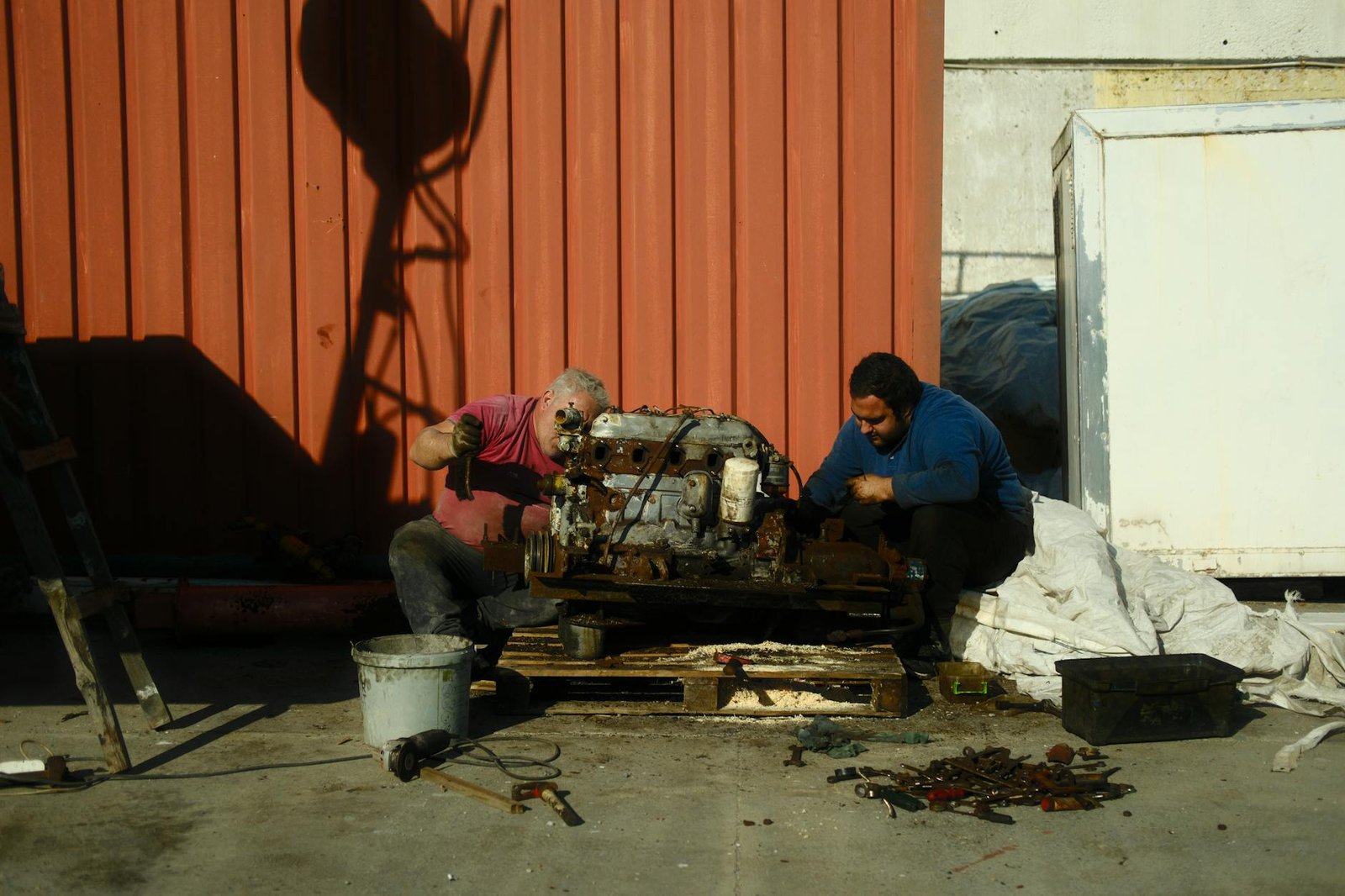 Fixing a Broken Stove: Step-by-Step Solutions for Common Issues 1 Two men repairing an engine outdoors, using tools and collaborating under a bright sunny sky.