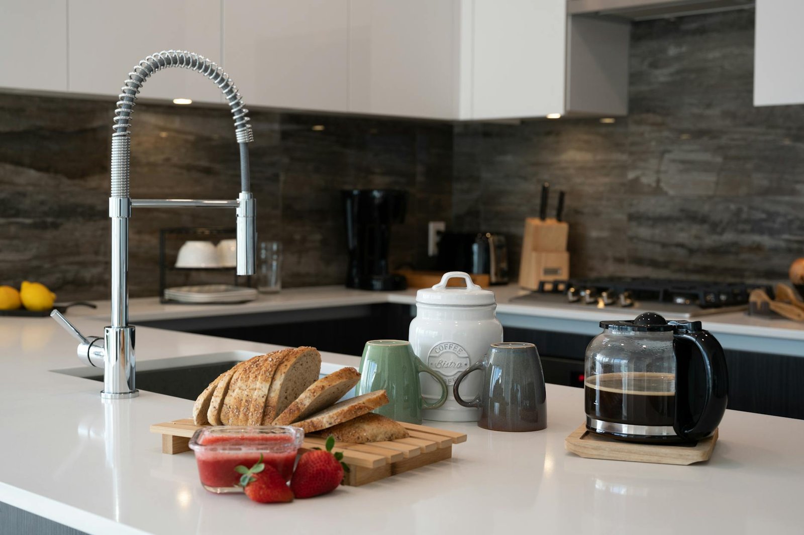 A modern kitchen interior with fresh bread, coffee pot, and strawberries on the counter.