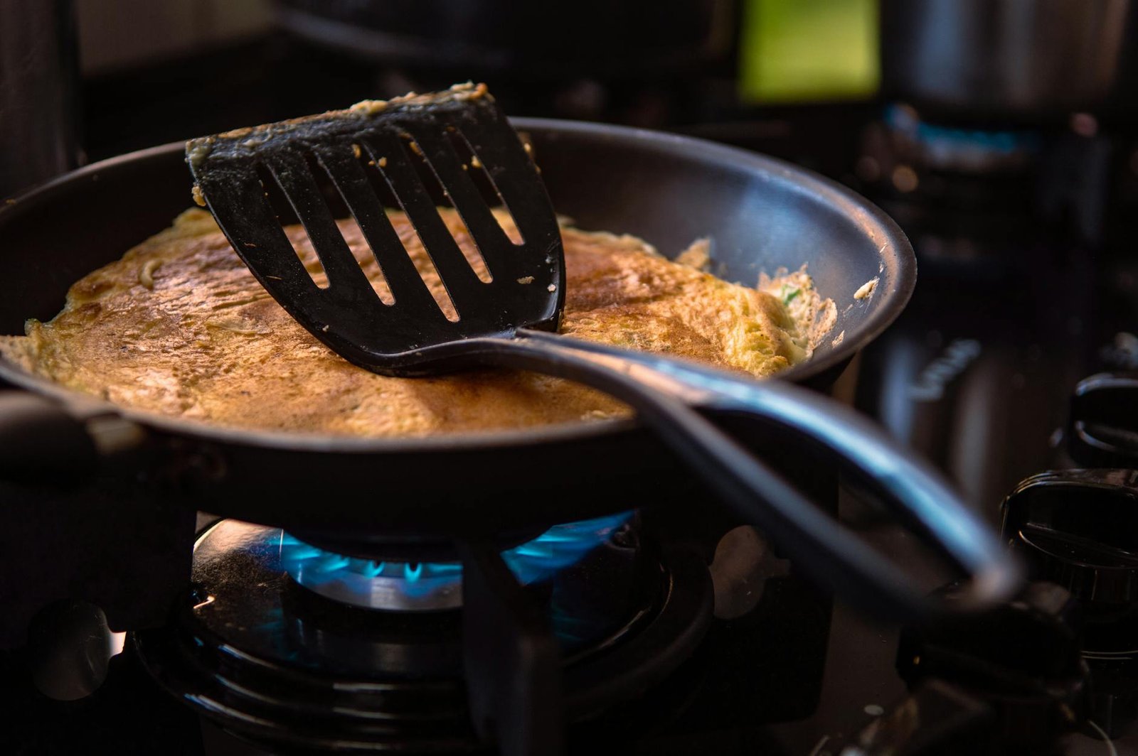 A perfectly cooked omelet in a frying pan with spatula on a kitchen stove.