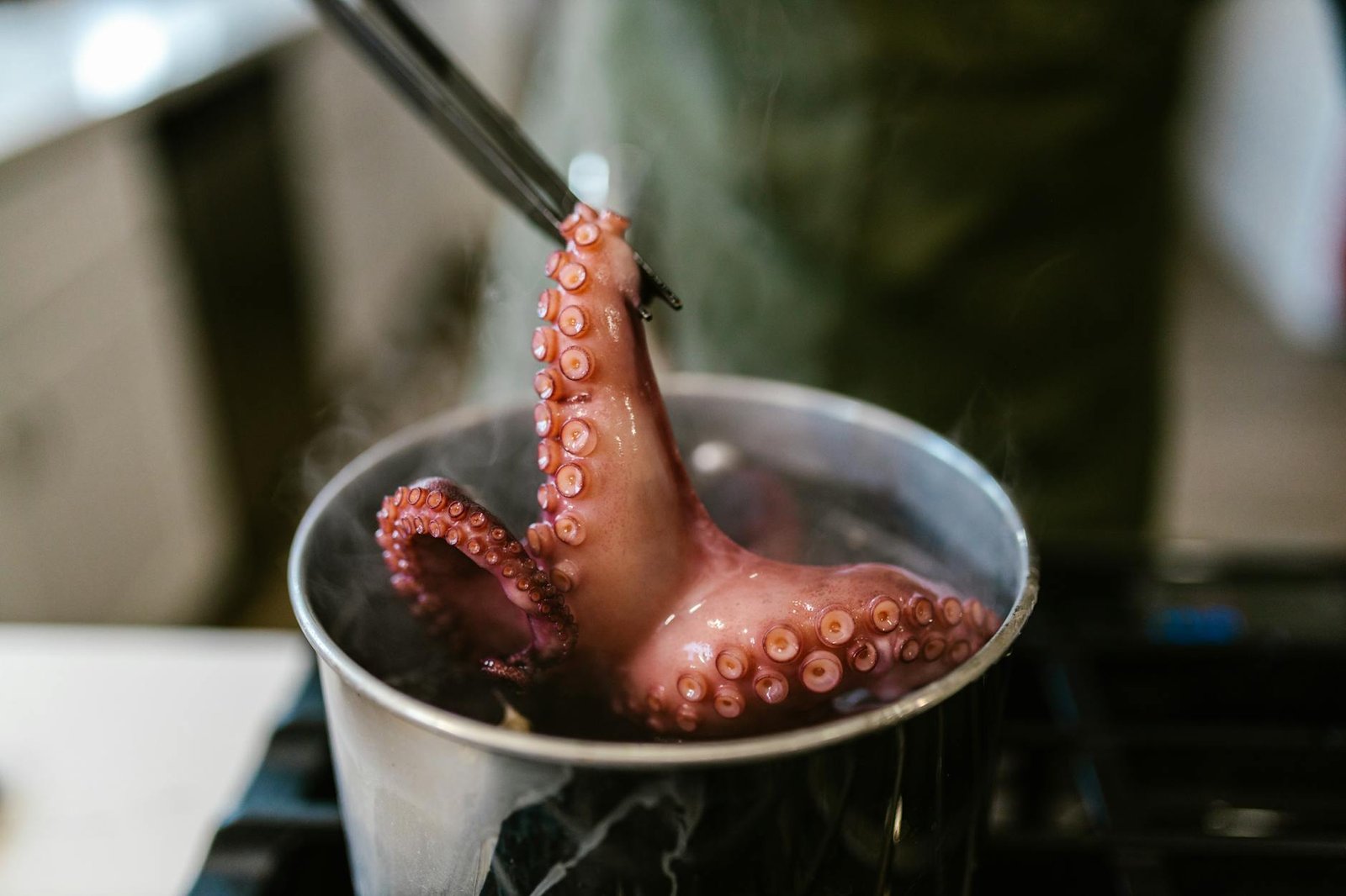 A close-up of an octopus being cooked in a pot on a stove, with steam rising.