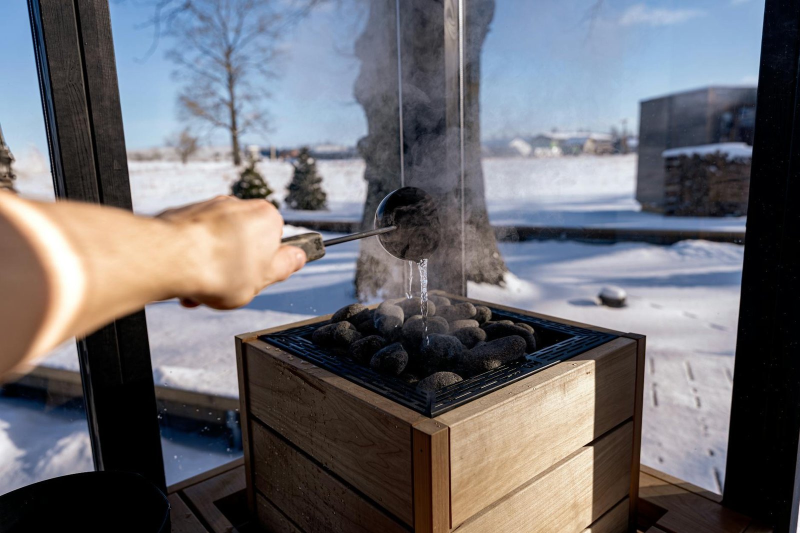 Steam rises from sauna stones as water is poured in a snowy Nordic setting, capturing a serene and warming experience.