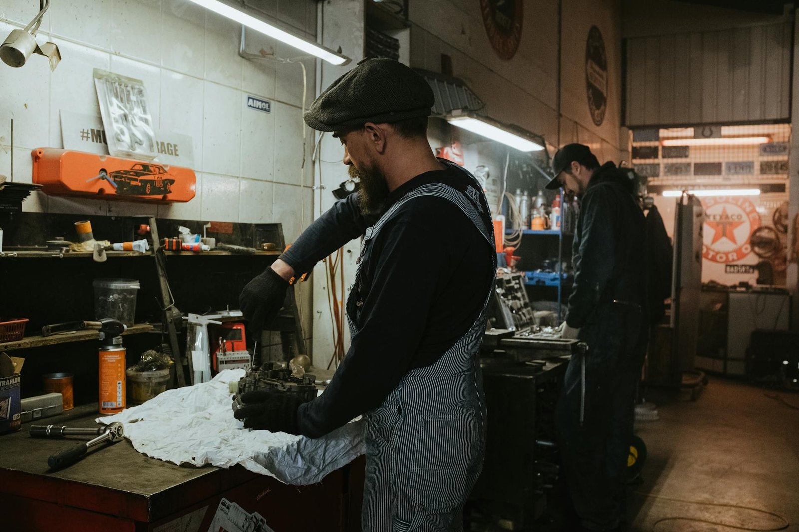 Two auto mechanics engaged in vehicle repair work inside a dimly lit garage.