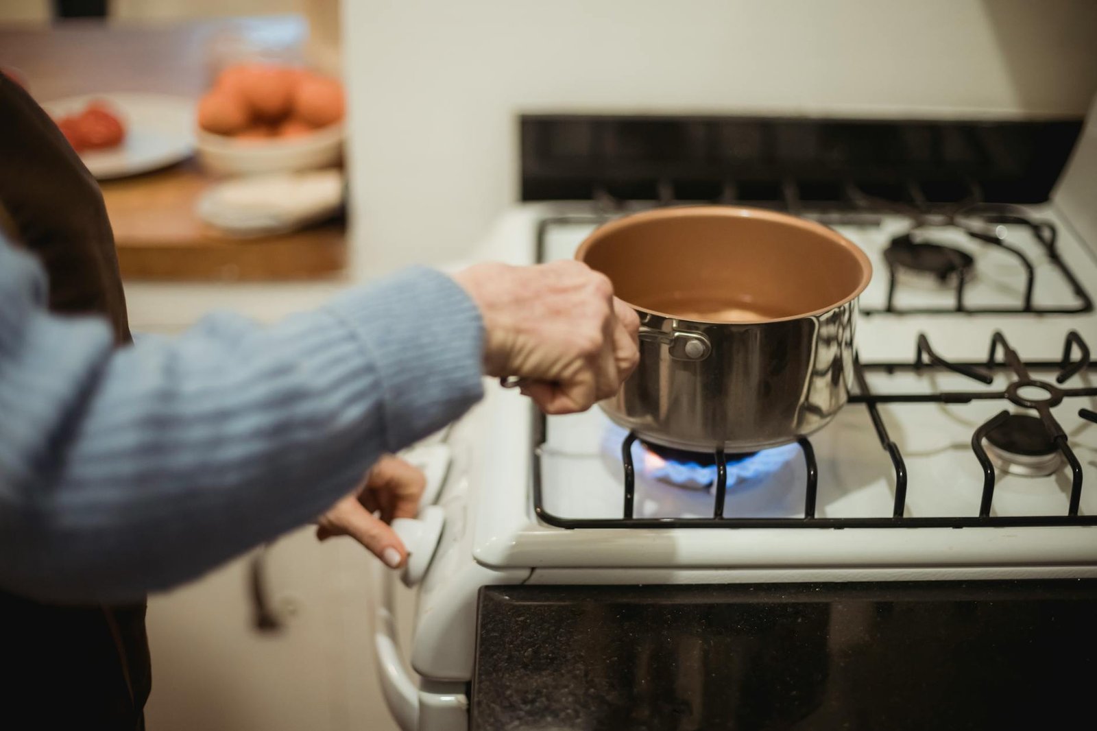 Gas Stove vs Electric Stove: How Heat Distribution Affects Your Cooking 3 A woman cooks using a saucepan on a modern gas stove indoors, showcasing domestic kitchen activity.