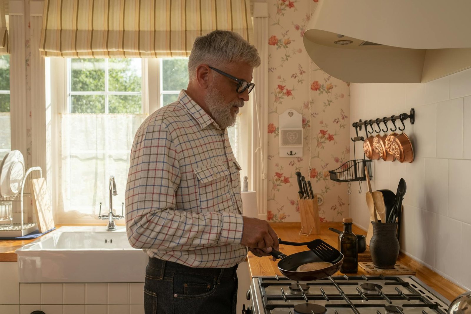 Senior man cooking pancakes in a warm, sunny kitchen setting.