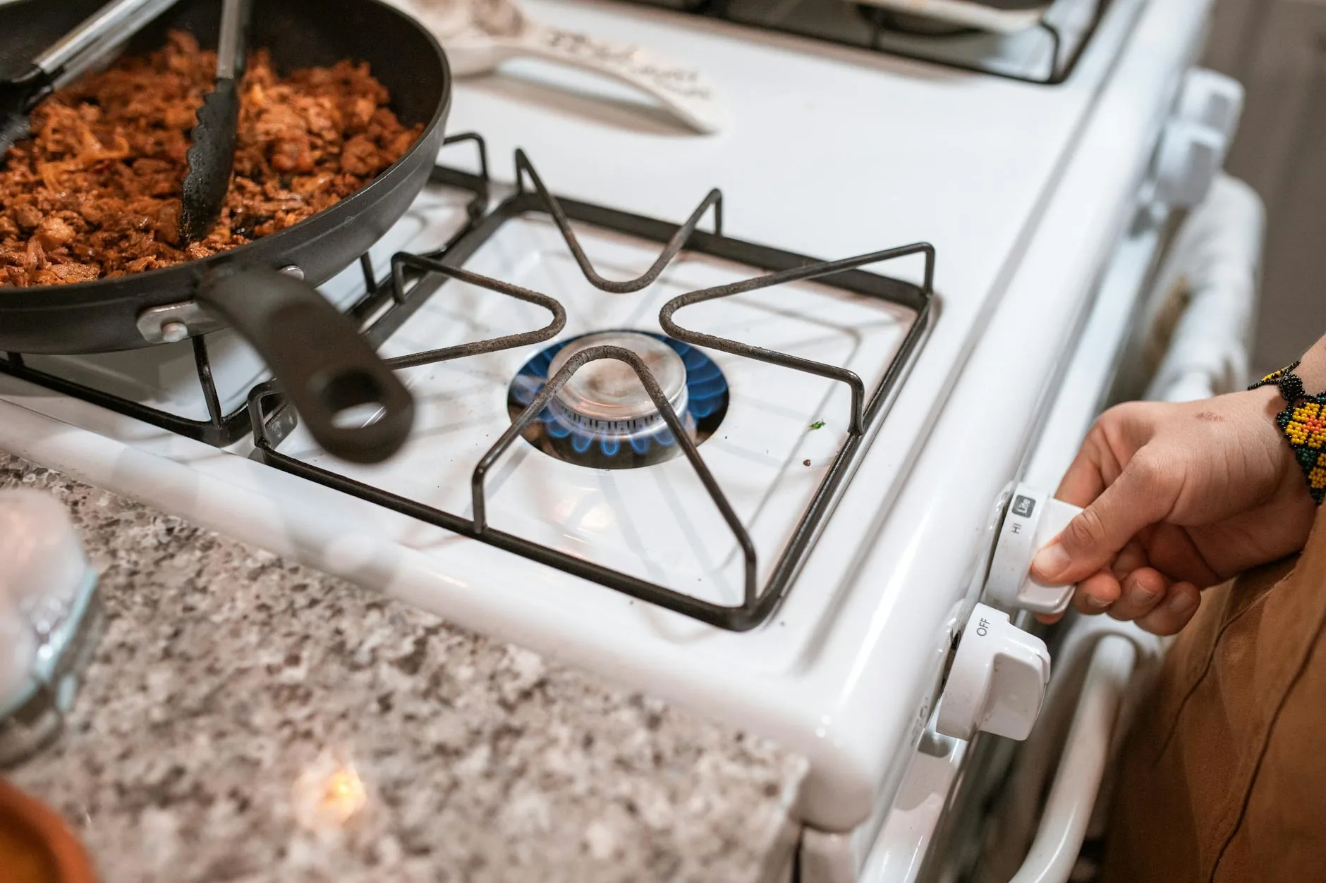 A hand turning a gas stove knob during safe cooking — modern auto-ignition stoves cut fuel automatically if a flame fails to establish