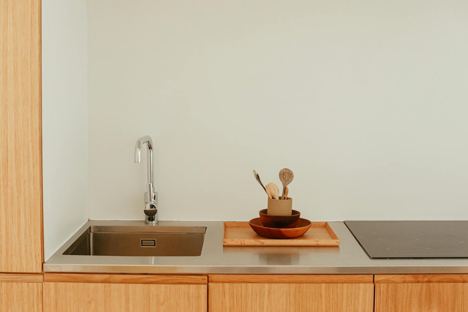 Simple and elegant kitchen counter with sink, faucet, wooden bowls, and induction stove.