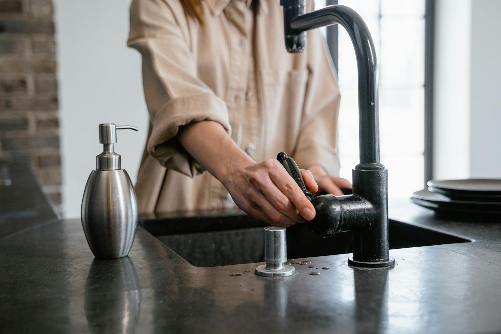 Close-up of a person washing hands at a black kitchen sink with a soap dispenser.