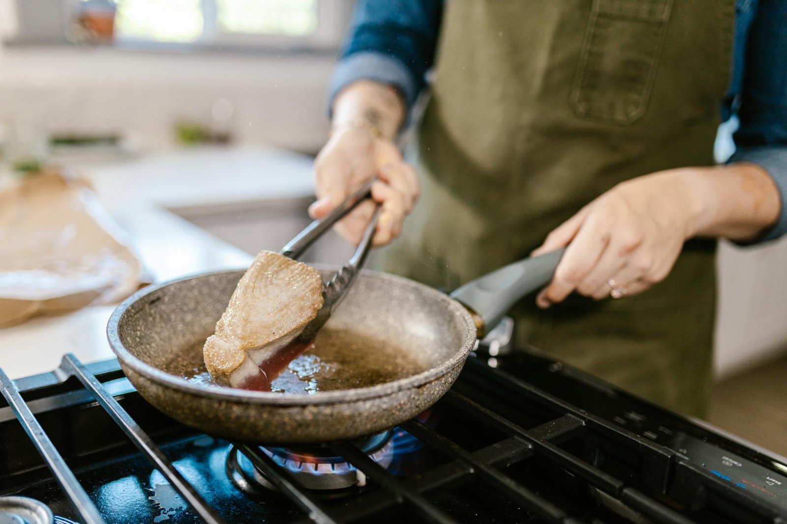 Kitchen Ventilation System Reviews for Apartment Dwellers 3 Close-up of a chef frying a tuna steak using tongs in a pan on a gas stove.