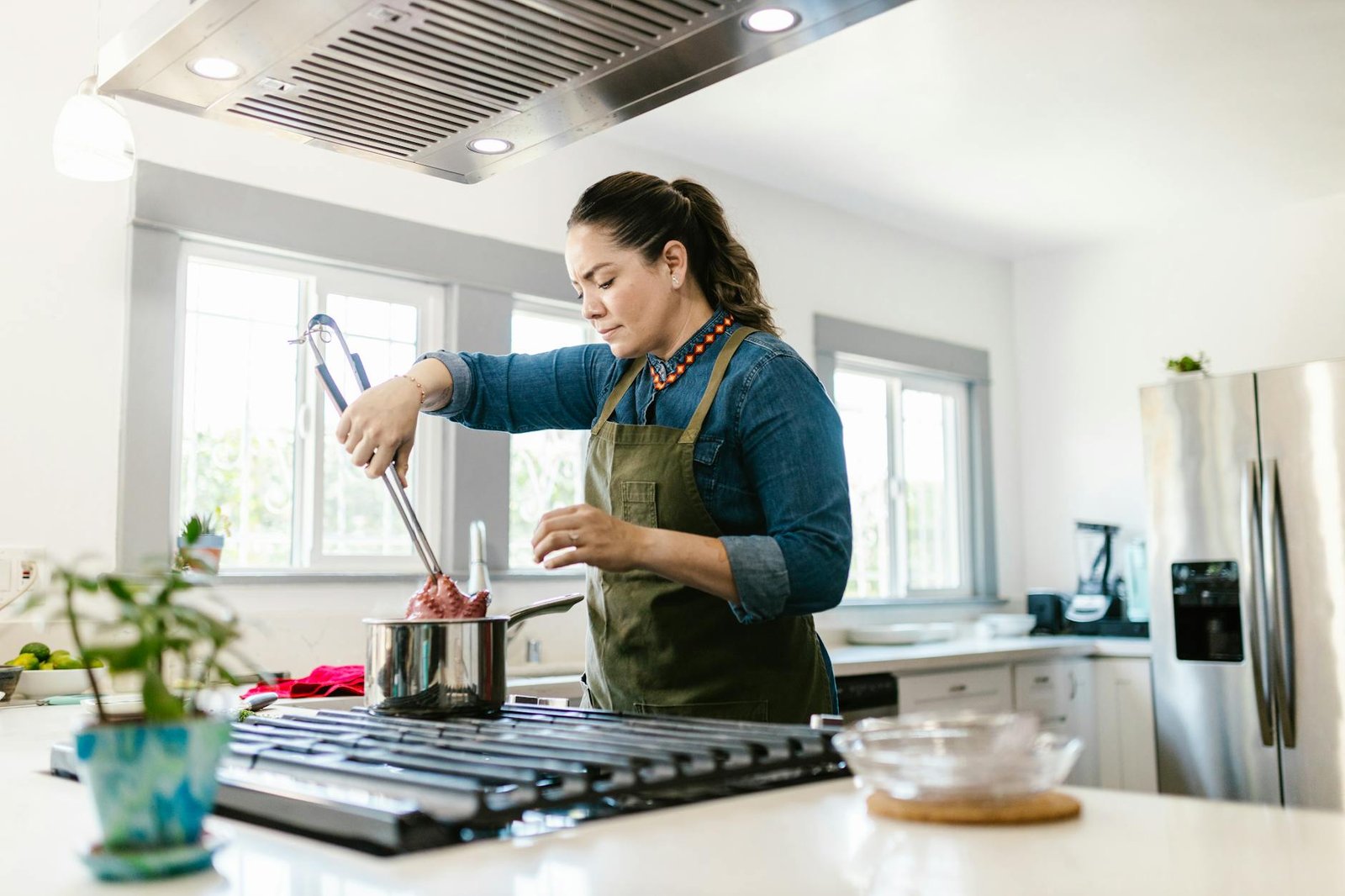 Adult woman preparing food on a stove in a bright, modern kitchen.
