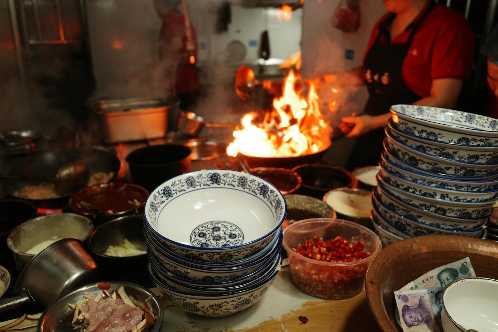 Vibrant street food scene in a Chinese kitchen with flames and stacked bowls.