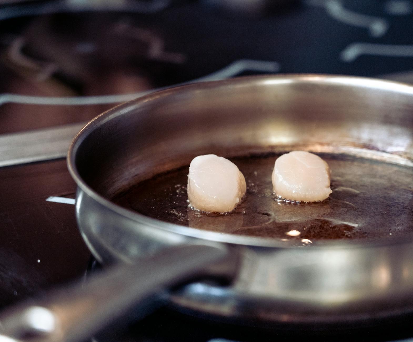 Close-up of scallops being seared in a stainless steel pan on a stovetop.