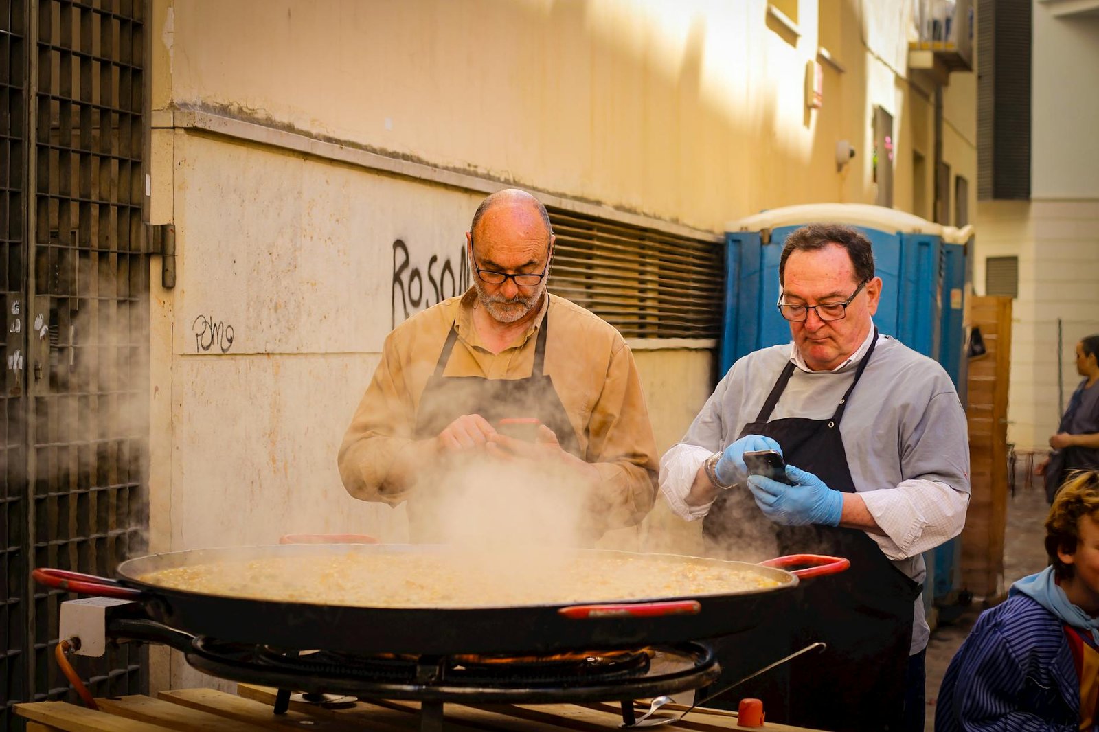 Optimizing Your Gas Stove for Efficient Cooking and Safety 11 Two chefs cook a large paella outdoors using a phone recipe.