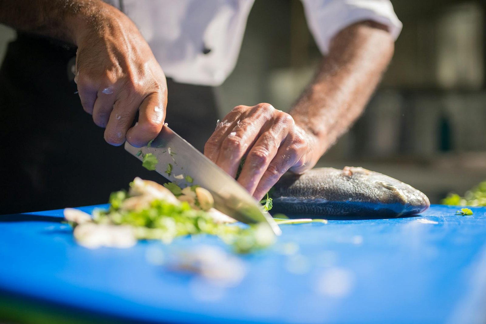 Optimizing Your Gas Stove for Efficient Cooking and Safety 2 Chef slicing fresh fish on a blue cutting board with herbs for culinary preparation.