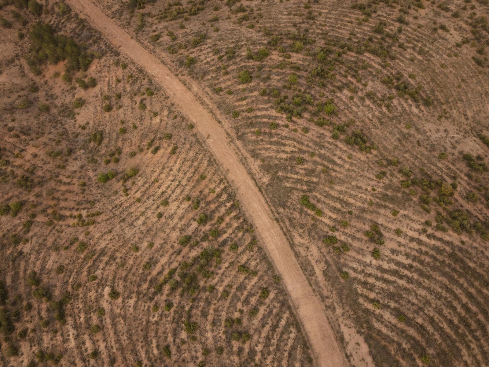 An aerial shot of a winding dirt road through a dry, rugged landscape.