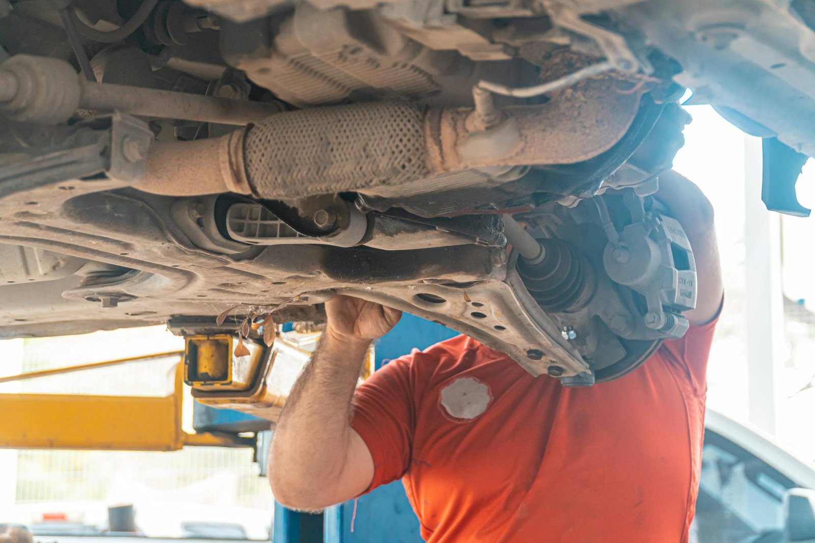 Mechanic working under a vehicle, inspecting the undercarriage in a repair garage, ensuring safety and performance.