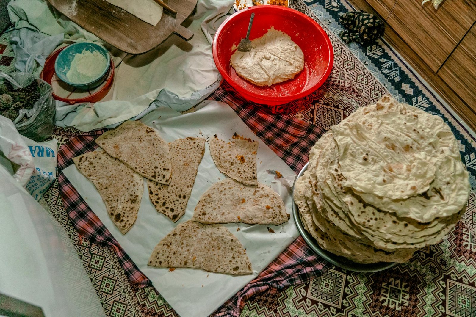 A cozy indoor scene of traditional Turkish flatbread preparation, showcasing dough and baked goods on a patterned tablecloth.