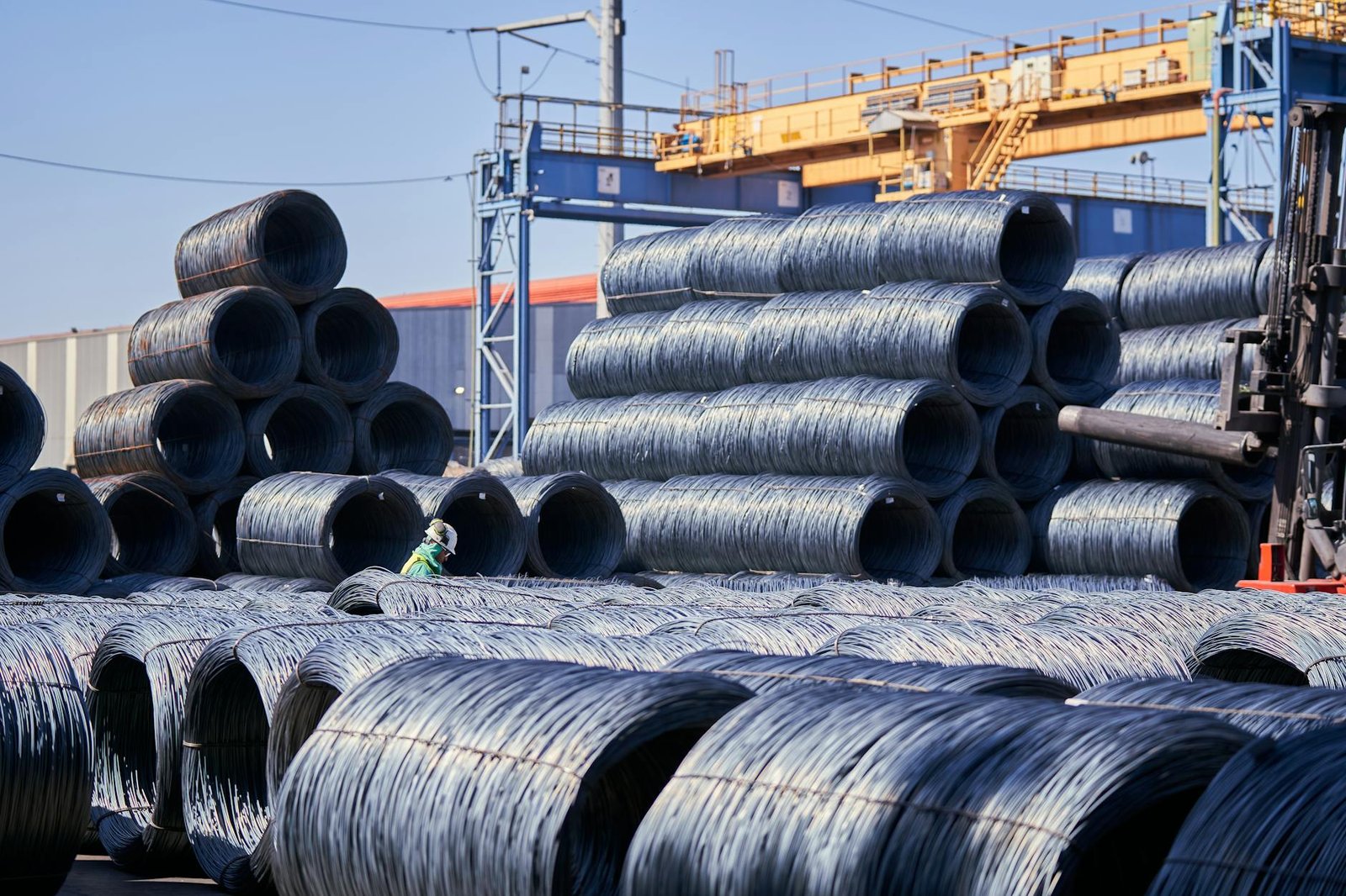 Large stacks of steel wire coils stored outdoors at an industrial site under bright daylight.