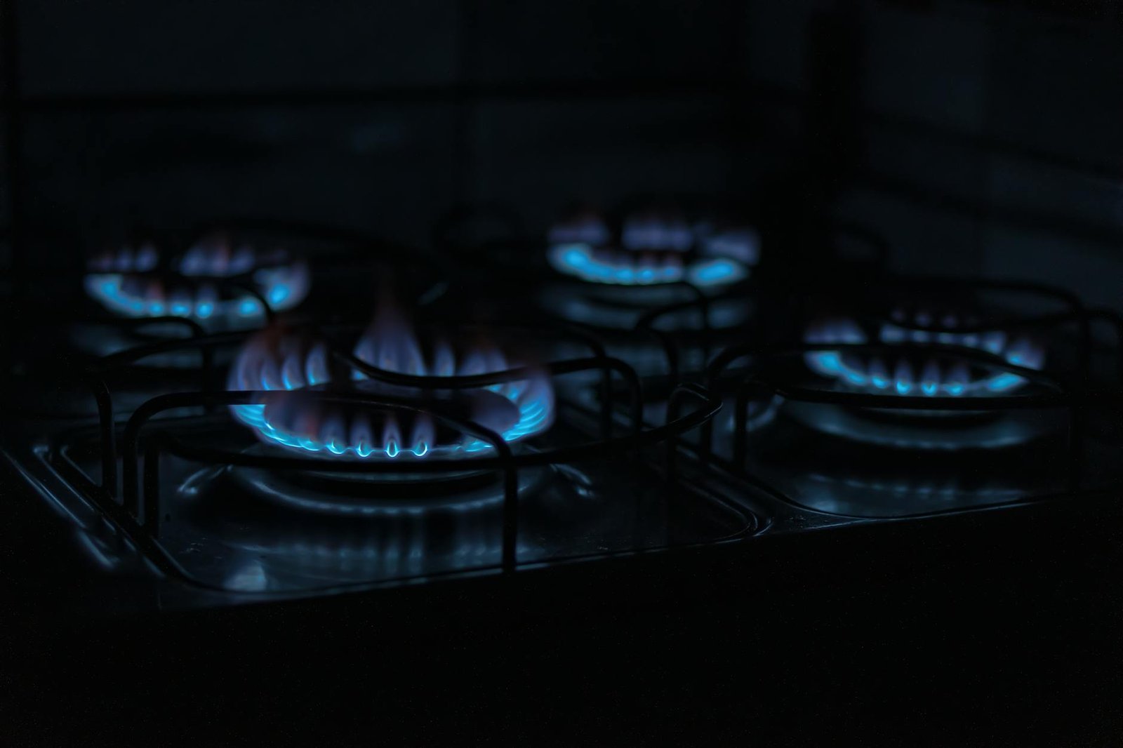 A dark, atmospheric image capturing the blue flames of gas stove burners indoors.