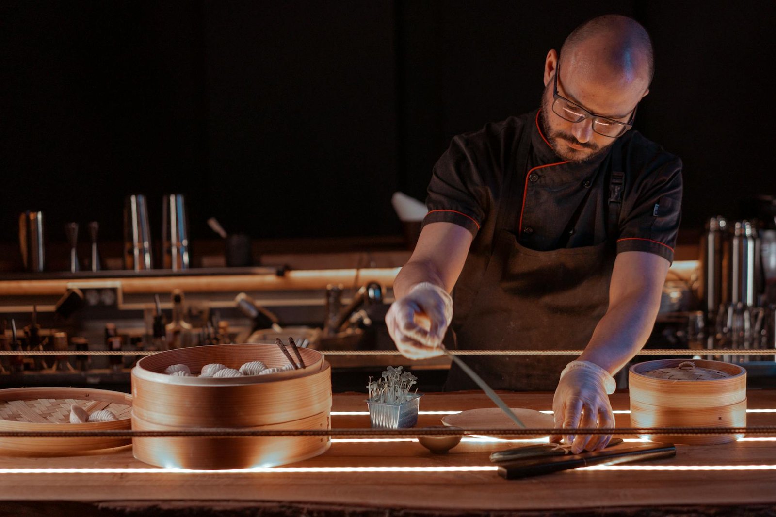 Chef in a restaurant kitchen preparing dumplings using bamboo steamers and chopsticks.