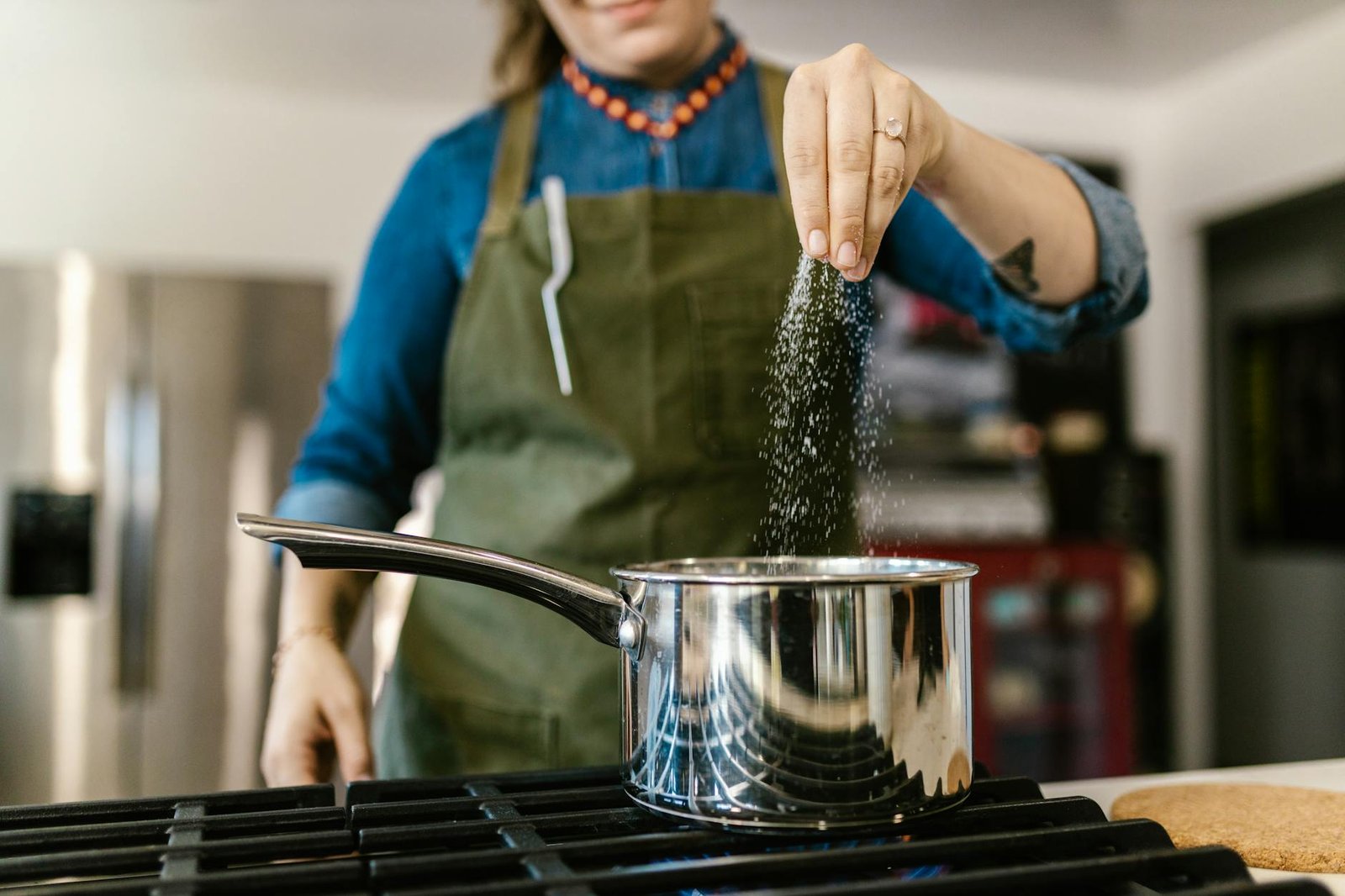 Close-up of a woman adding salt to a pot on a stove in a modern kitchen setting.