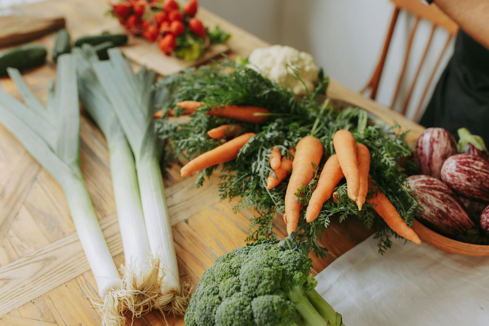 Colorful variety of fresh vegetables including carrots, broccoli, and leeks arranged on a wooden table.